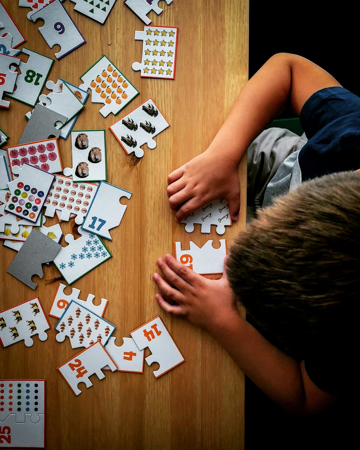 Dziecko bawi się edukacyjnymi puzzlami z cyframi na drewnianym stole.